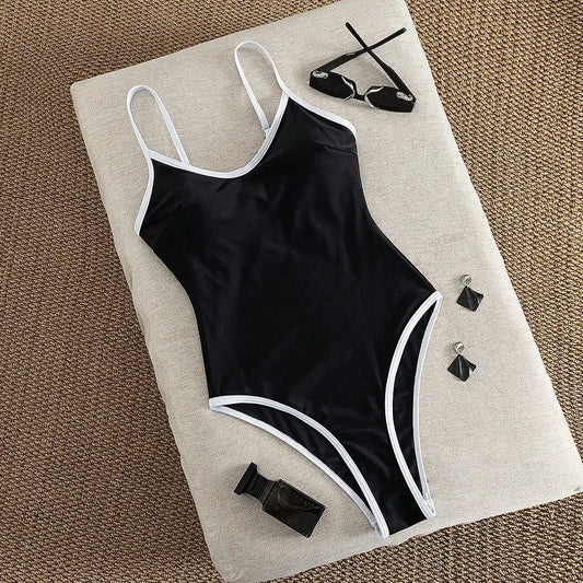 Costume intero da donna nero con finiture bianche, scollatura sulla schiena, taglio alto e sgambato, ideale per l'estate e le vacanze al mare.