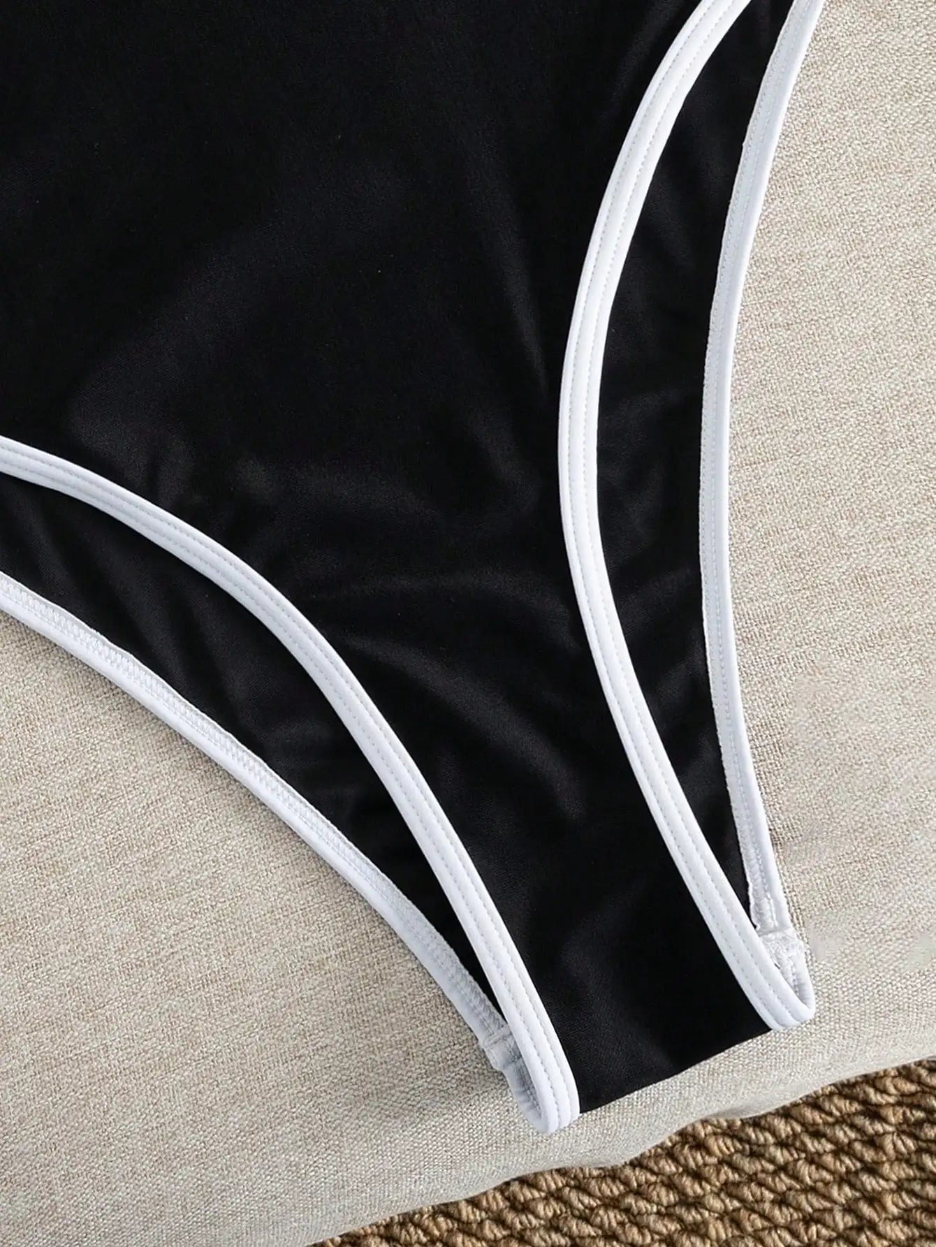 Costume intero da donna nero con finiture bianche, scollatura sulla schiena, taglio alto e sgambato, ideale per l'estate e le vacanze al mare.